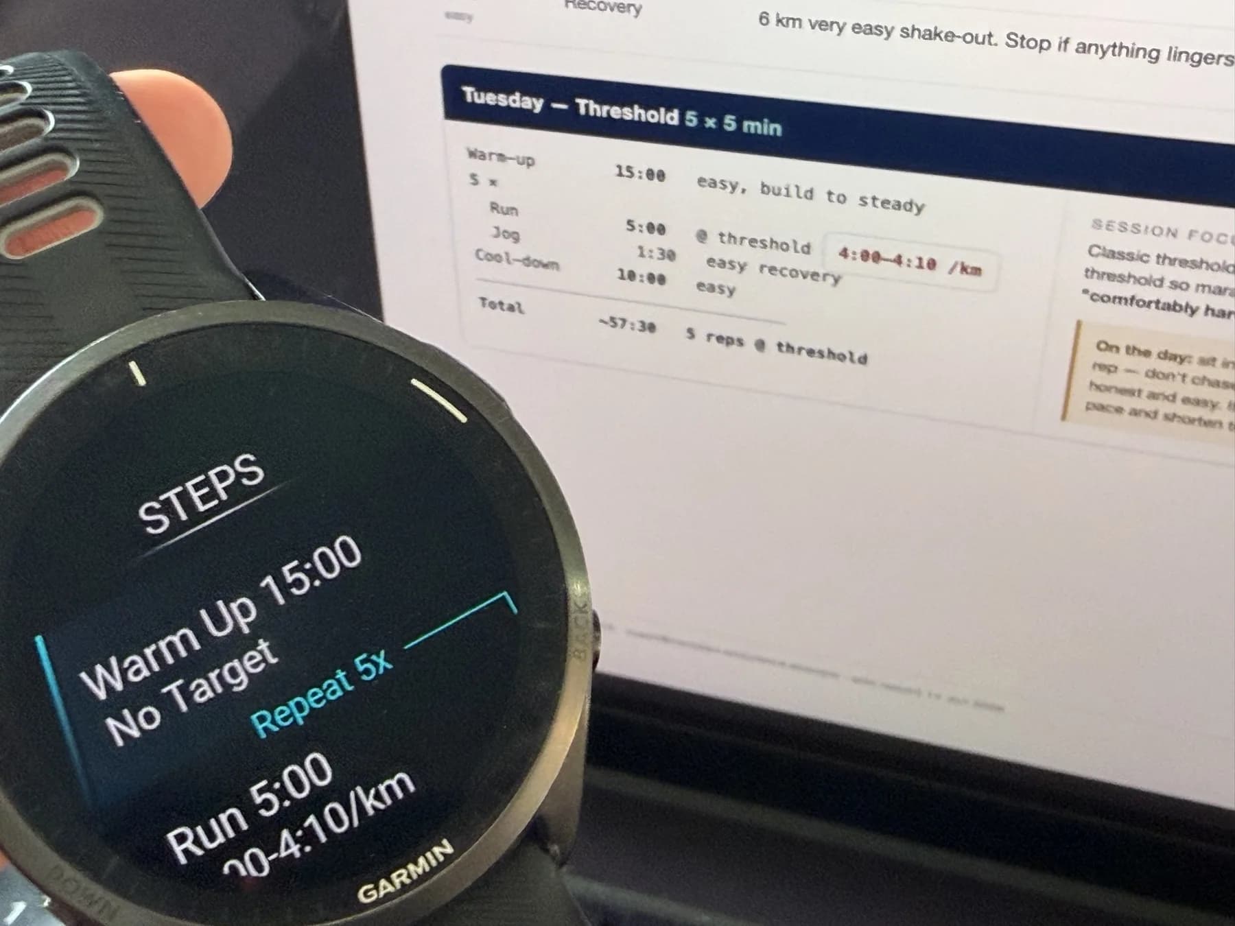 A coach's printed training plan beside a Garmin Forerunner 965 showing the same session as structured steps – warm-up 15:00, repeat 5×, run 5:00 at 4:00–4:10/km.